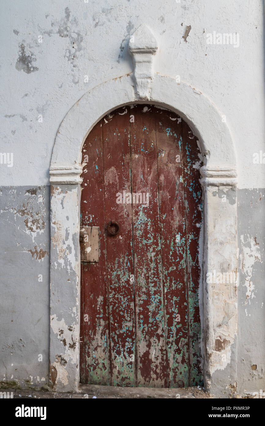 Old wooden brown gate with a visible original green painting. White and grey combination of the wall of the house. Rabat - Sale, Morocco. Stock Photo