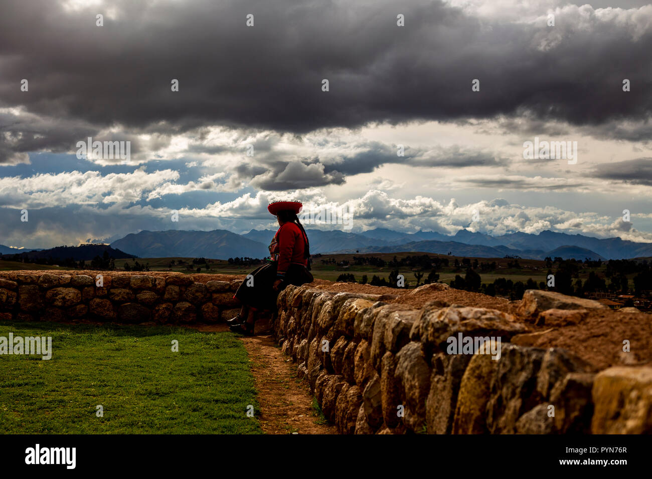 Einwohnerin eines peruanischen Dorfes sitzt auf Steinmauer und schaut auf den Horizont , Peru , Südamerika Stock Photo