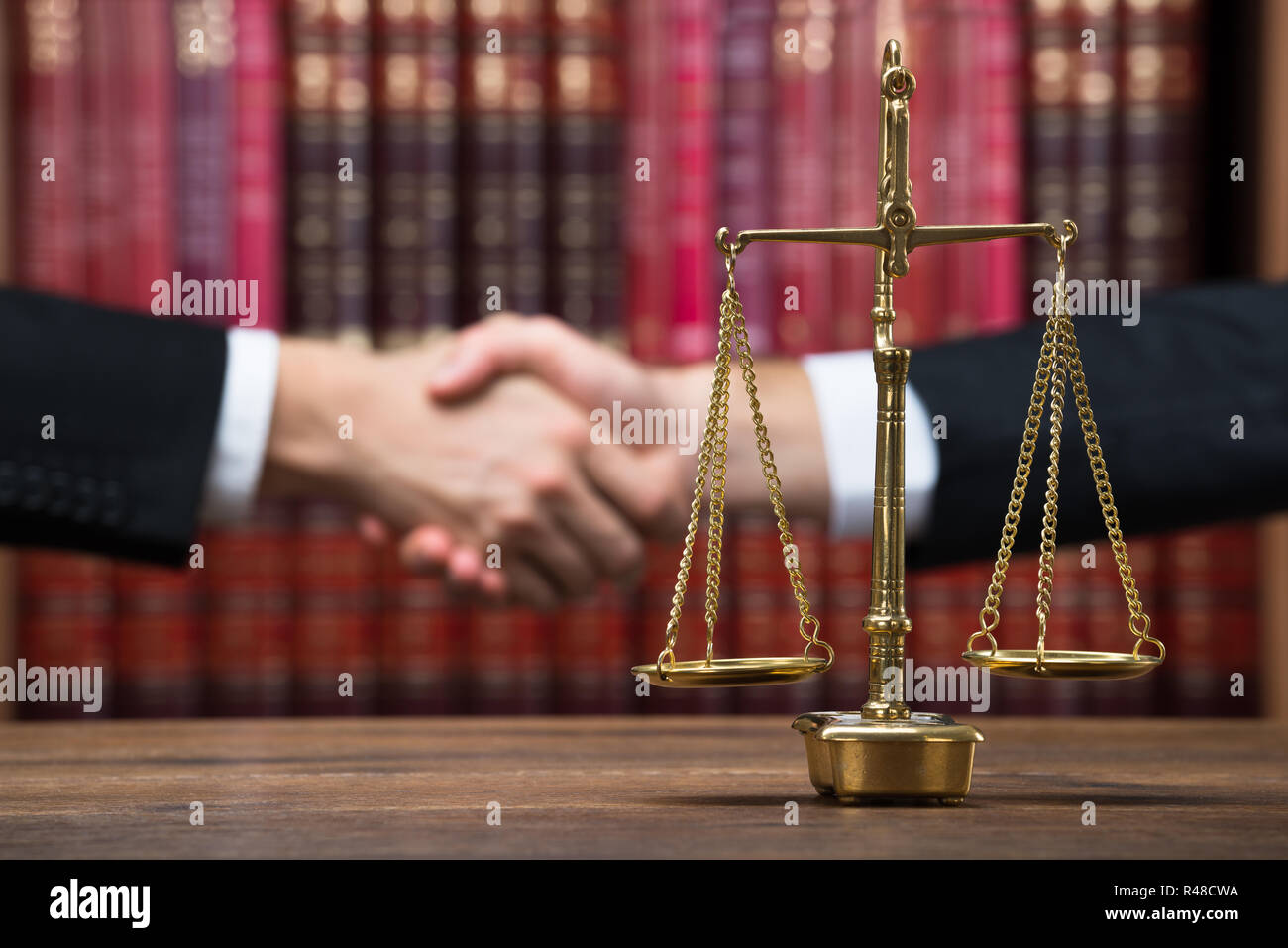 Justice Scale On Table With Judge And Client Shaking Hands Stock Photo