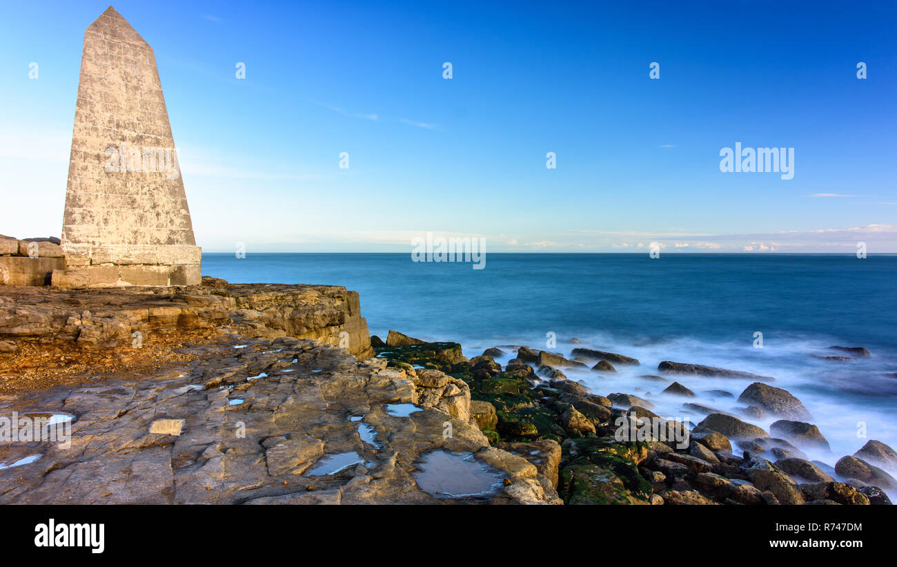 Waves crash on the rocky shore of the English Channel's Jurassic Coast under the Trinity House Obelisk marking the tip of Portland Bill in Dorset. Stock Photo