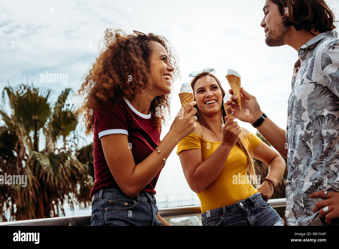 Smiling men and woman eating ice cream cone outdoors. Diverse group of friends eating ice-cream outdoors. Stock Photo