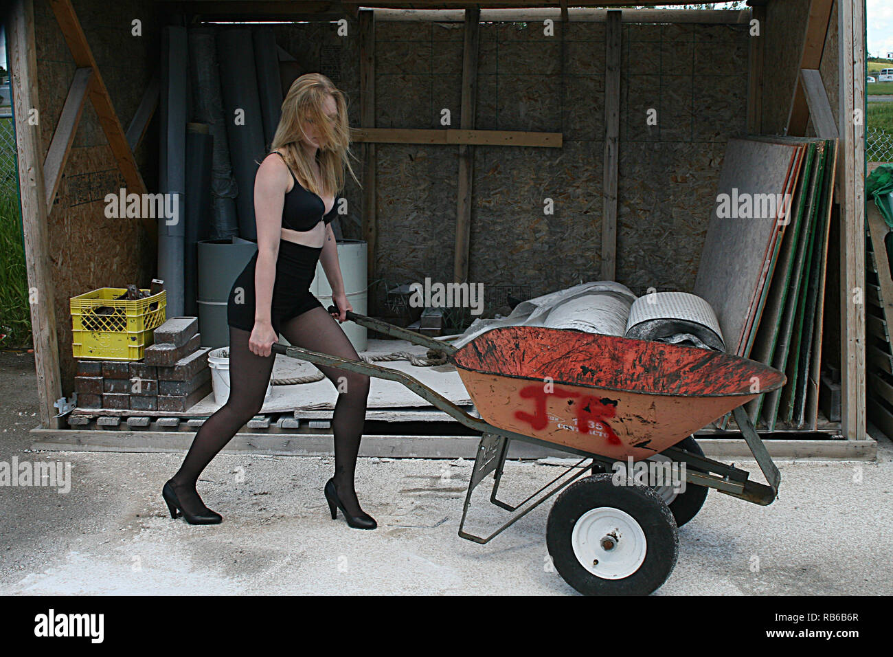 Blonde  Woman  wearing nylon stocking, high heels and short shorts pushing a wheel barrow Stock Photo