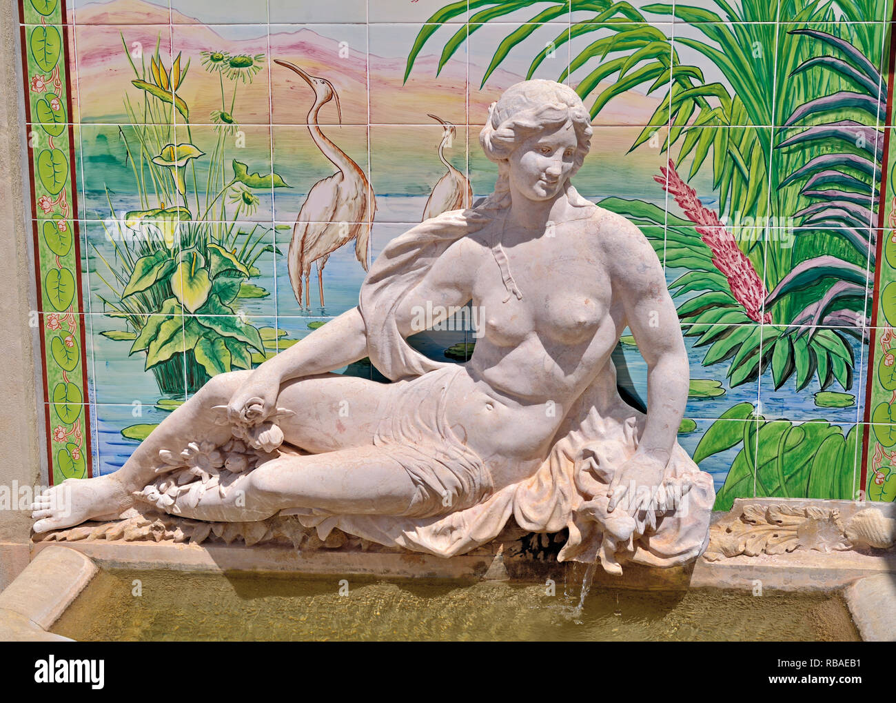 Statue of mythological figure in front of painted tiles with exotic scenery Stock Photo