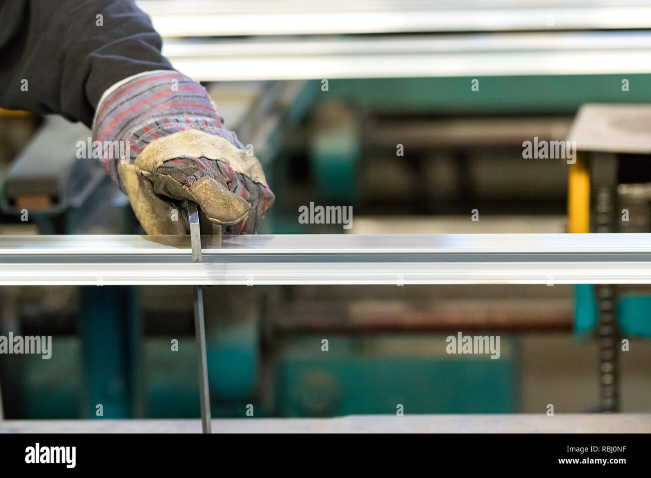 A man machine operator using safety gloves controlling the stretch of an aluminium profile with a squad. Stock Photo