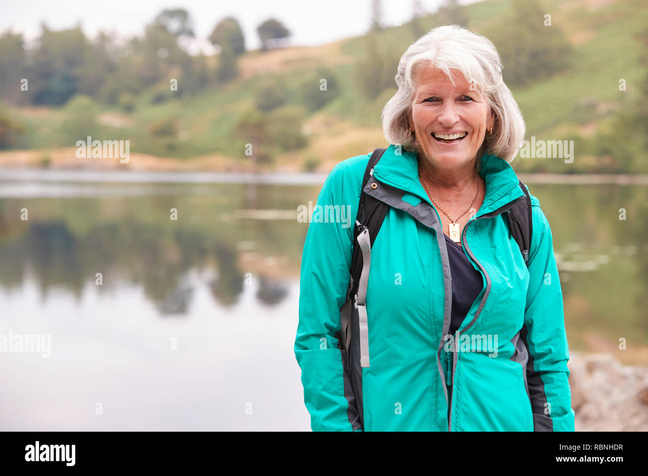 Senior Caucasian woman standing on a shore of a lake smiling to camera, portrait Stock Photo