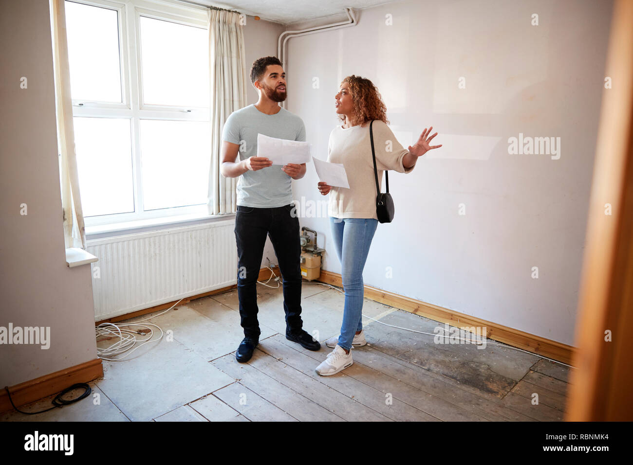 Couple Buying House For First Time Looking At House Survey In Room To Be Renovated Stock Photo