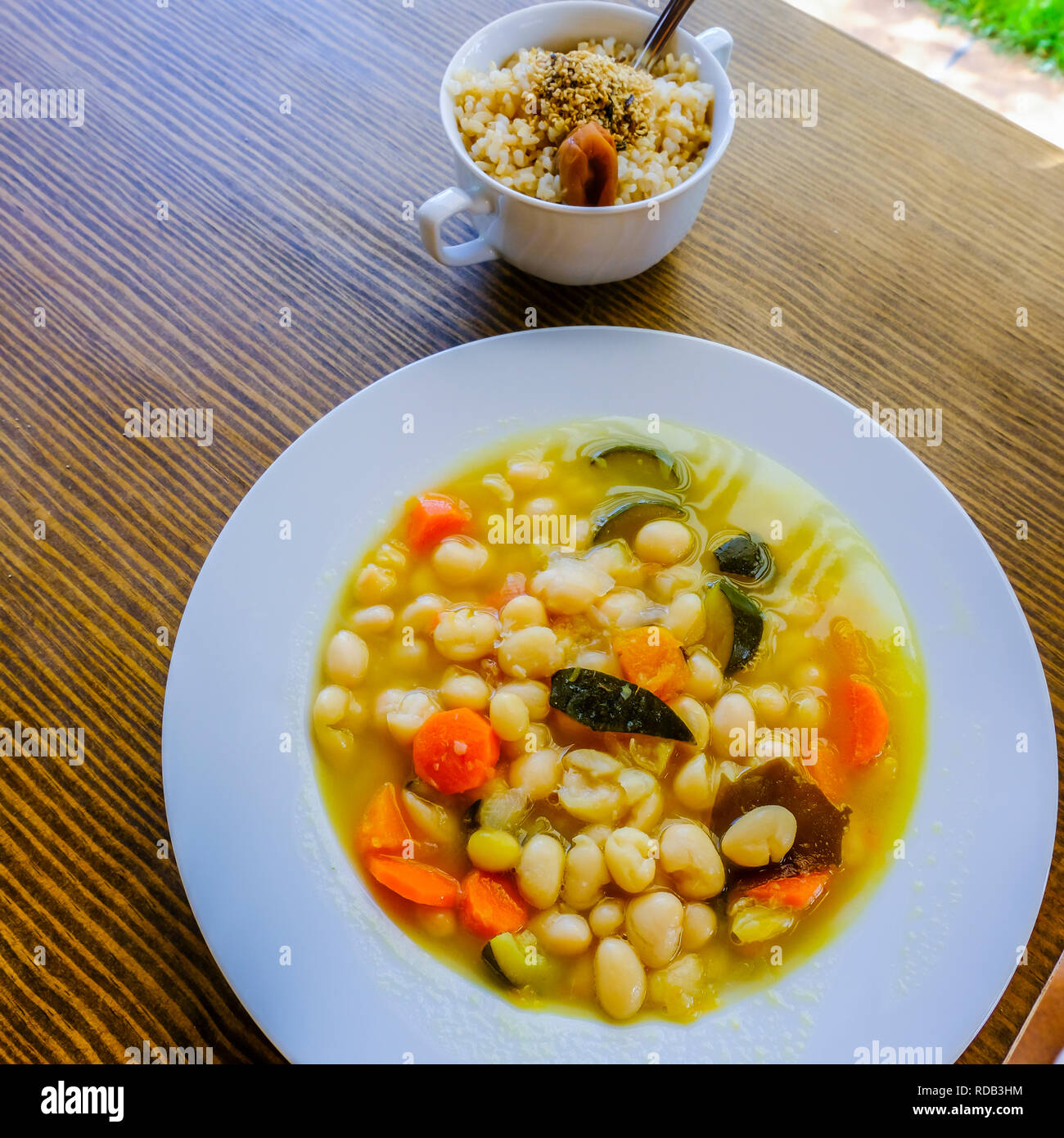 Pochas (Spanish string bean) with vegetables and kombu kelp (edible alga) and a cup of  brown rice with umeboshi (japanese pickled ume fruits). Macrob Stock Photo