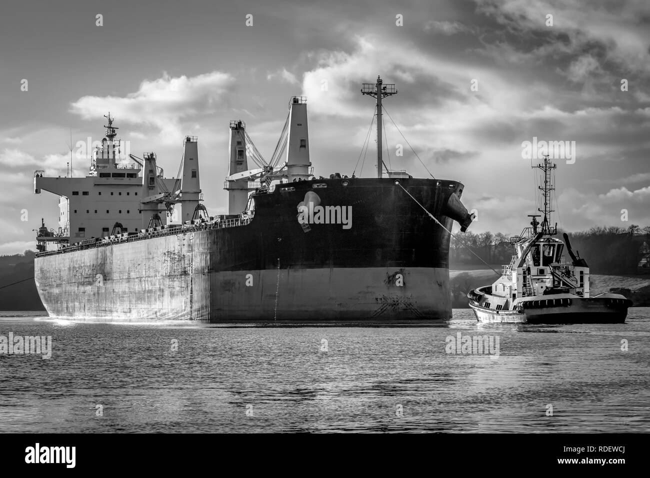 A picture of a cargo ship coming into habour being towed by a tug boat Stock Photo