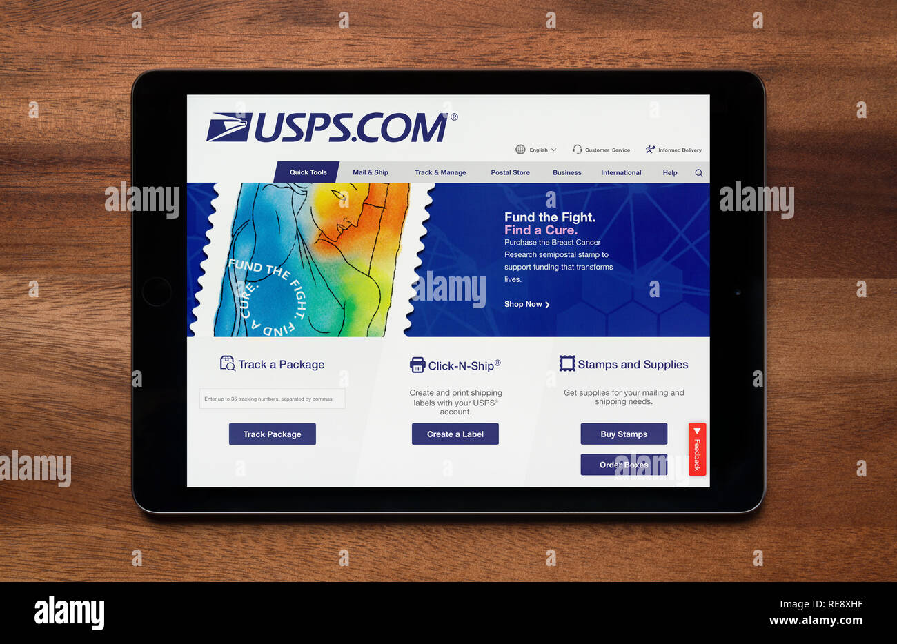 The website of USPS is seen on an iPad tablet, which is resting on a wooden table (Editorial use only). Stock Photo