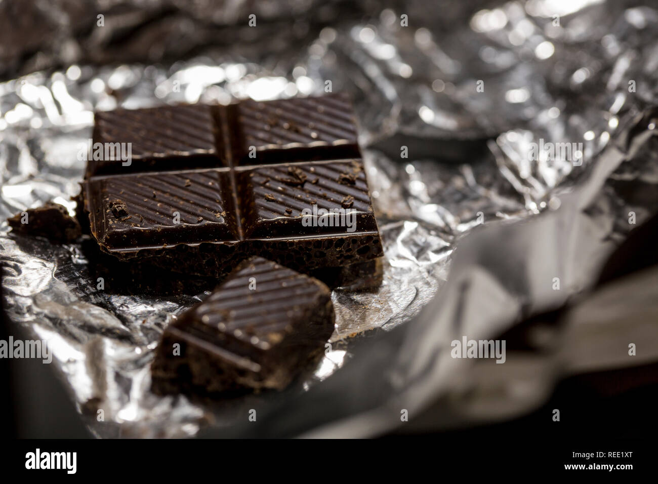 Macro photo of dark chocolate pieces in foil wrapper. Stock Photo