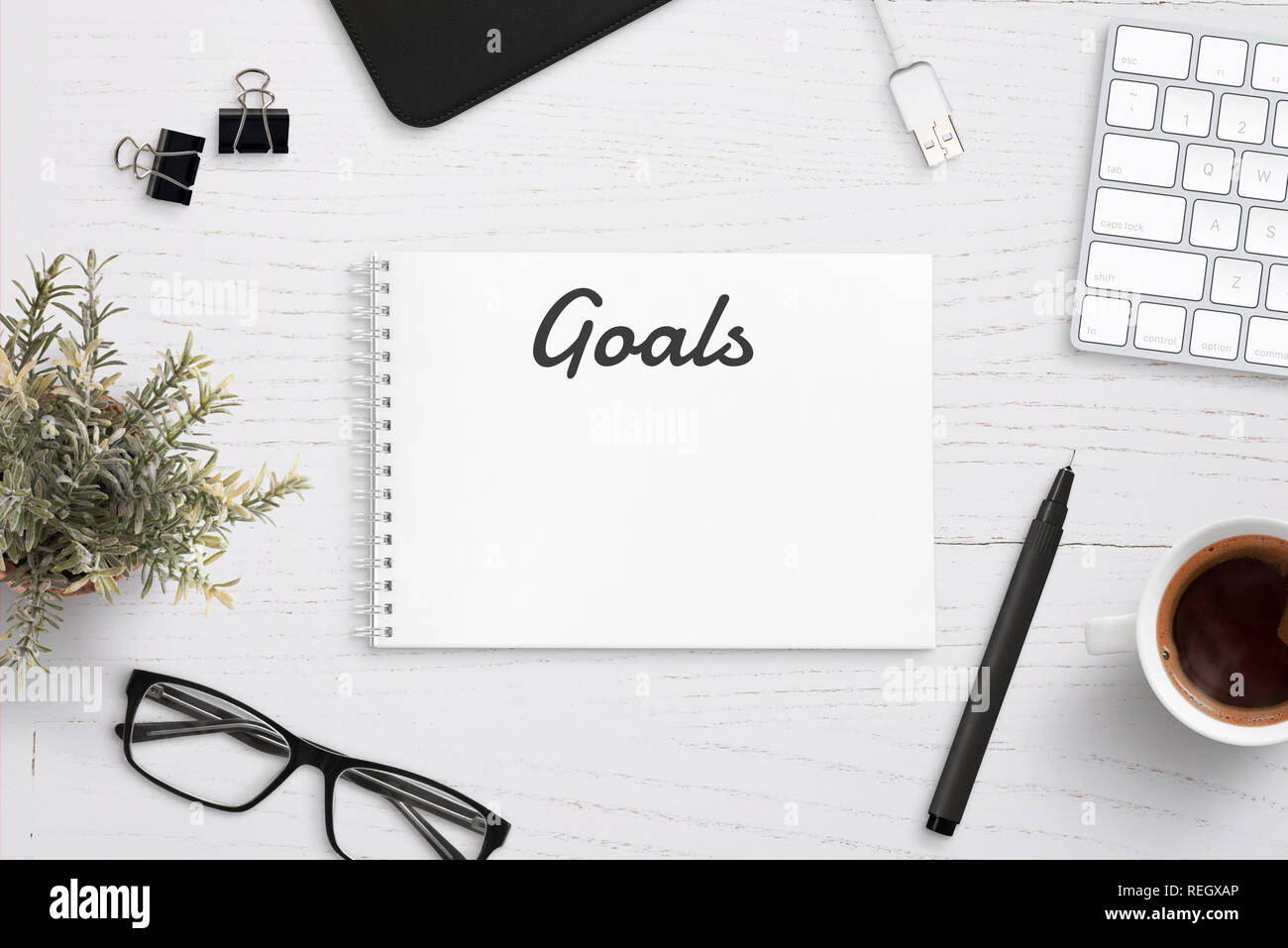 Creating goals list on notepad on office desk surrounded with office ...