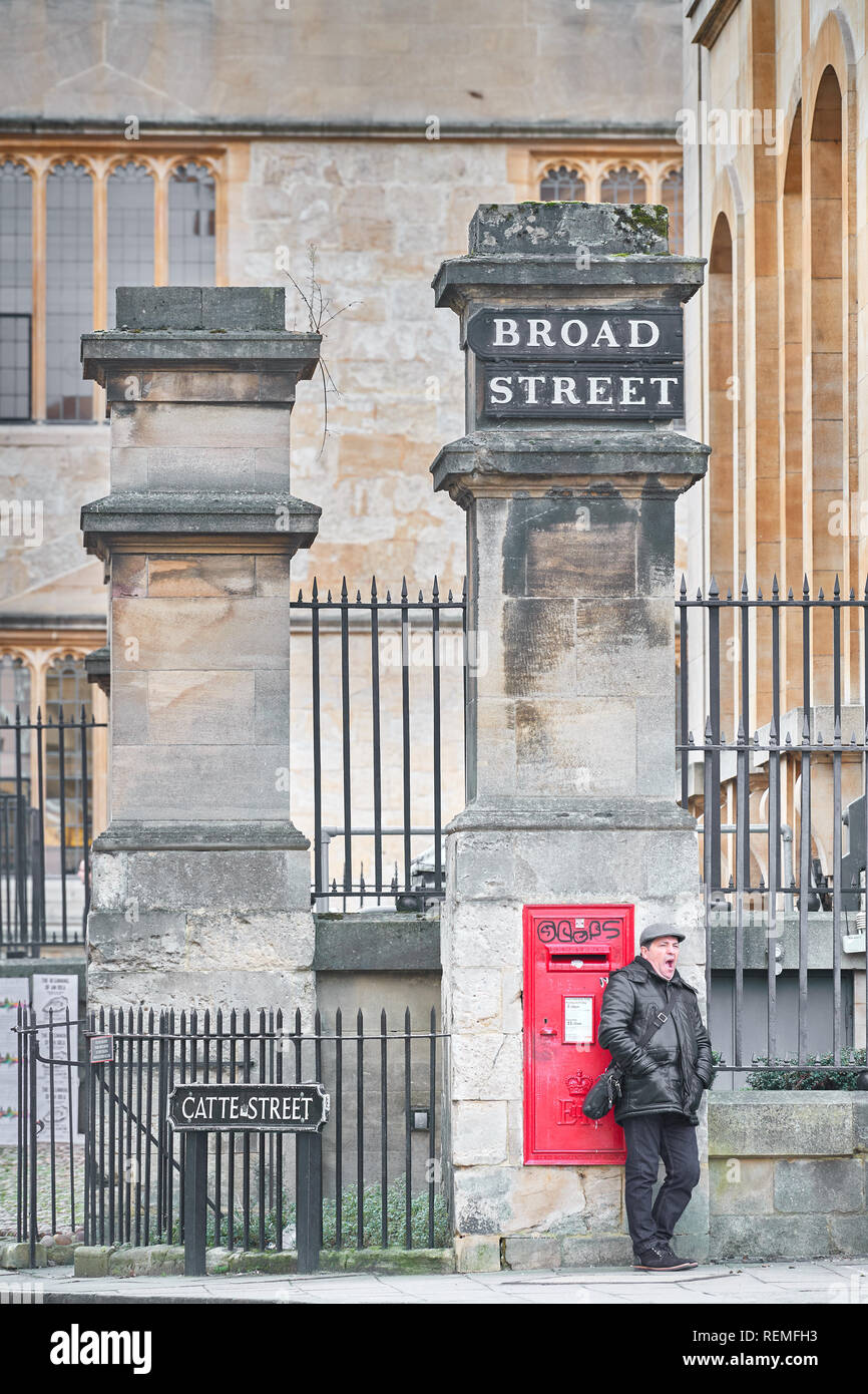 A man yawns whilst waiting next to a red post box outside the Clarendon building of the Bodleian library at the junction of Broad street and Catte st Stock Photo