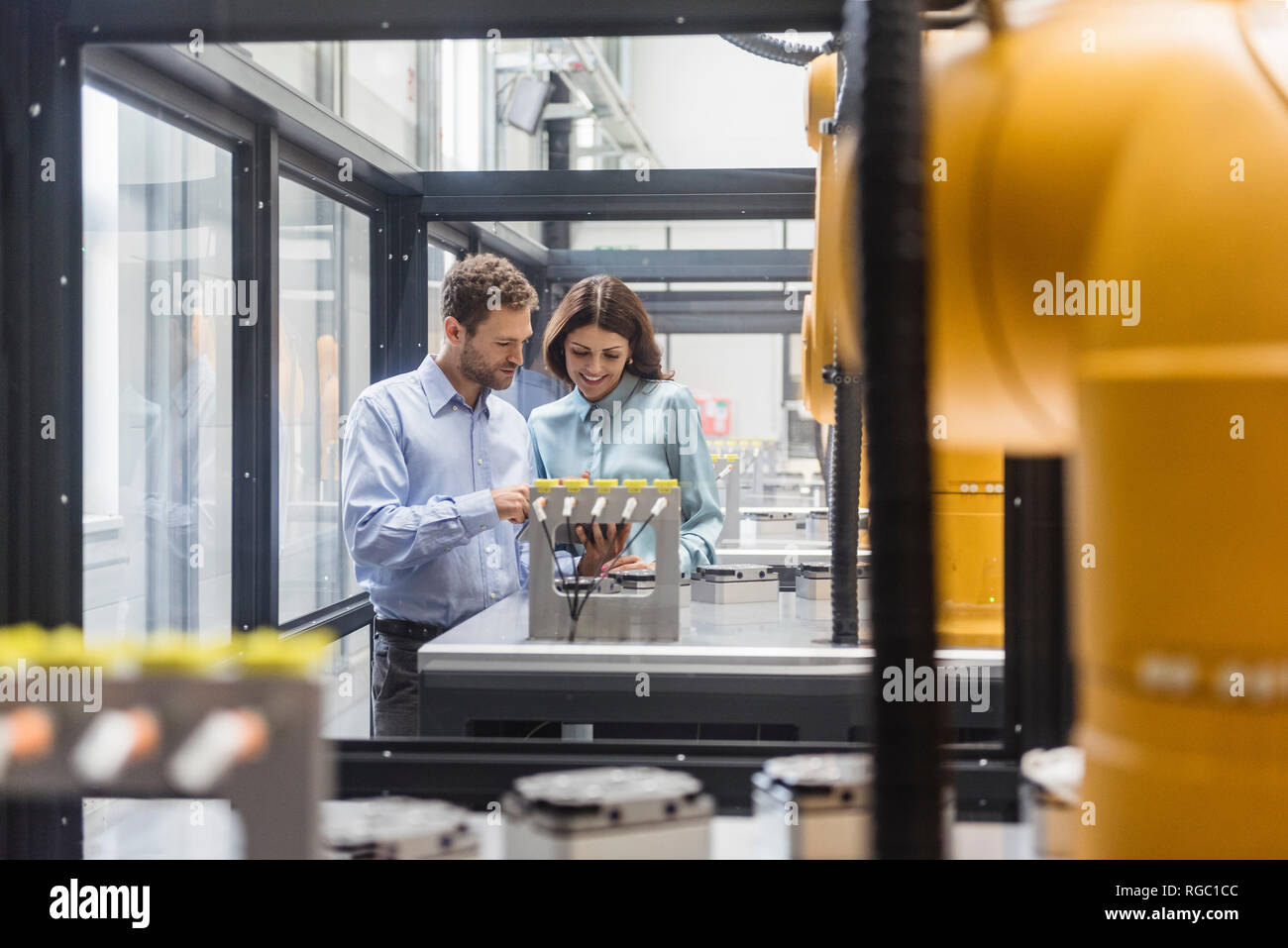 Colleagues in high tech company controlling industrial robots, using digital tablet Stock Photo