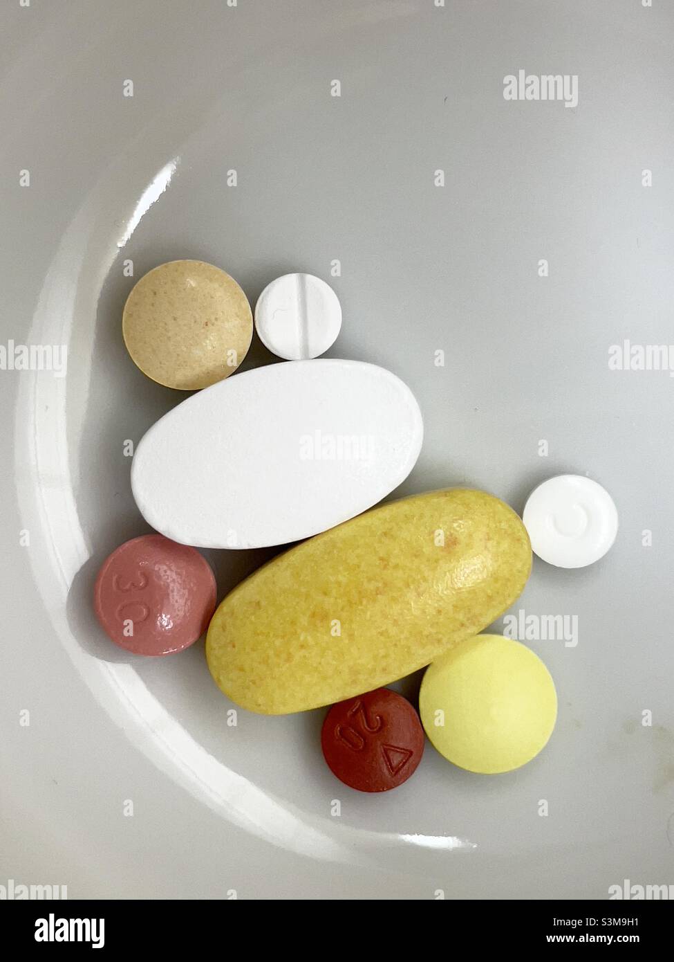 An assortment of pills round and oval in a small white ceramic bowl Stock Photo