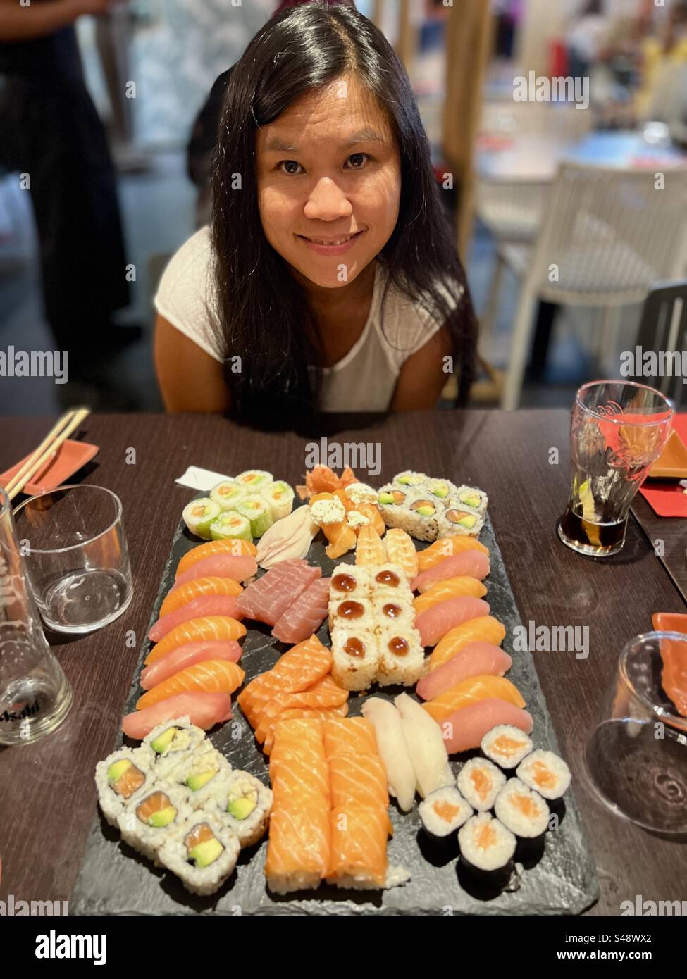 Cute Young Asian Filipino woman posing and smiling in front of a large sushi and sashimi platter in a Japanese restaurant in Montpellier, France. Stock Photo