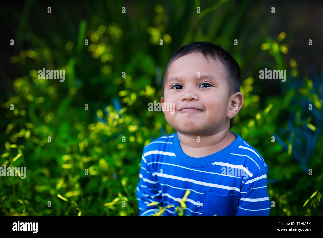 A healthy boy looking up in admiration with a positive attitude and satisfied smile sitting in a field of yellow wild flowers while wearing a striped  Stock Photo