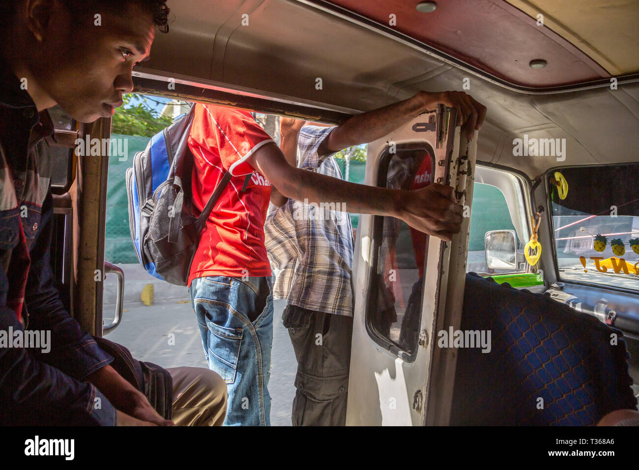 Dili, Timor-Leste - Aug 10, 2015: A teenage boy and other men inside a mikrolet bus driving with an open door, East Timor. Micro let minibus dangerous Stock Photo