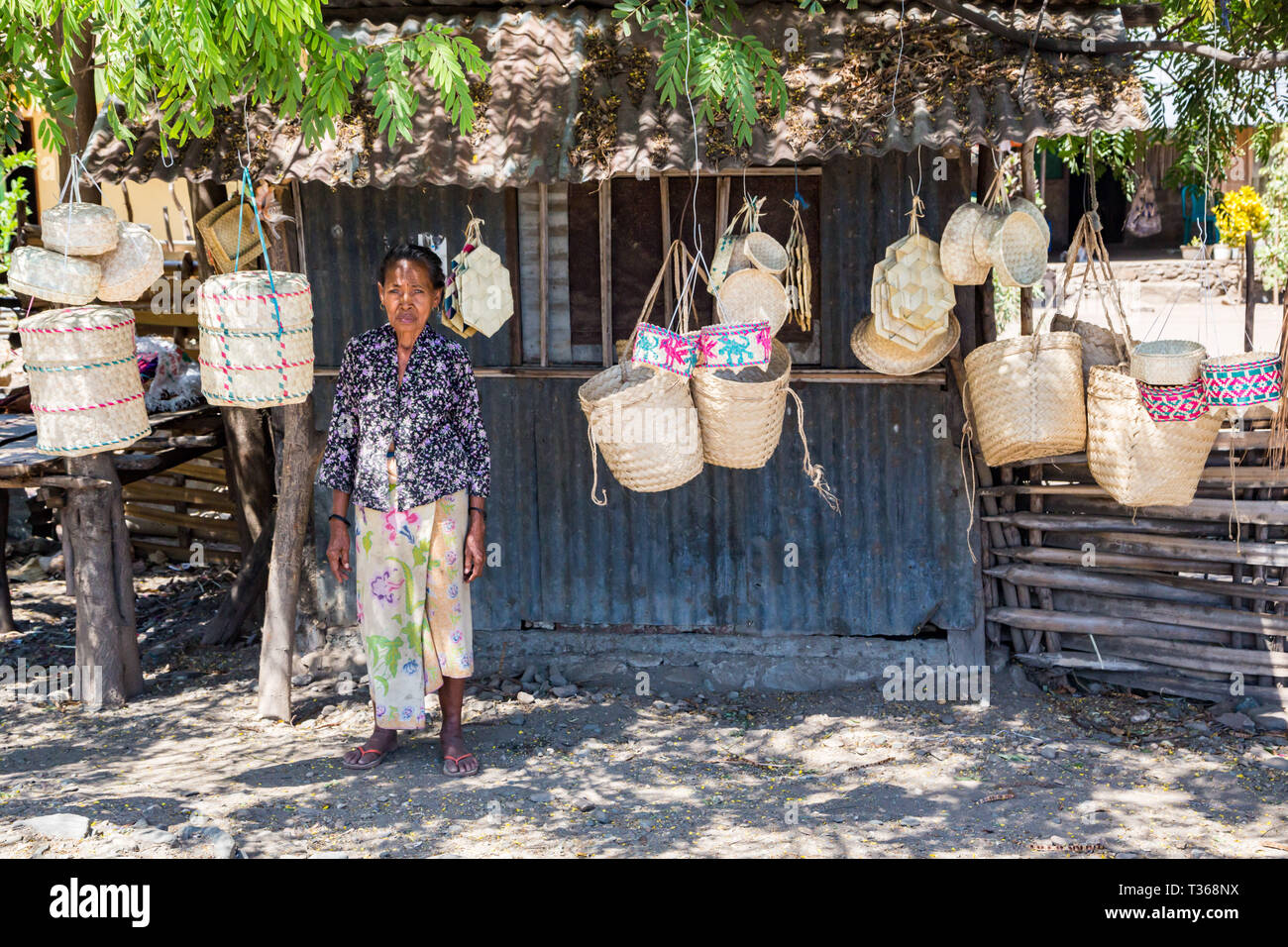 Dili, Timor-Leste - Aug 11, 2015: Local elderly native East Timorese woman, street vending traditional wicker baskets hanging on ropes, at a tin hut u Stock Photo