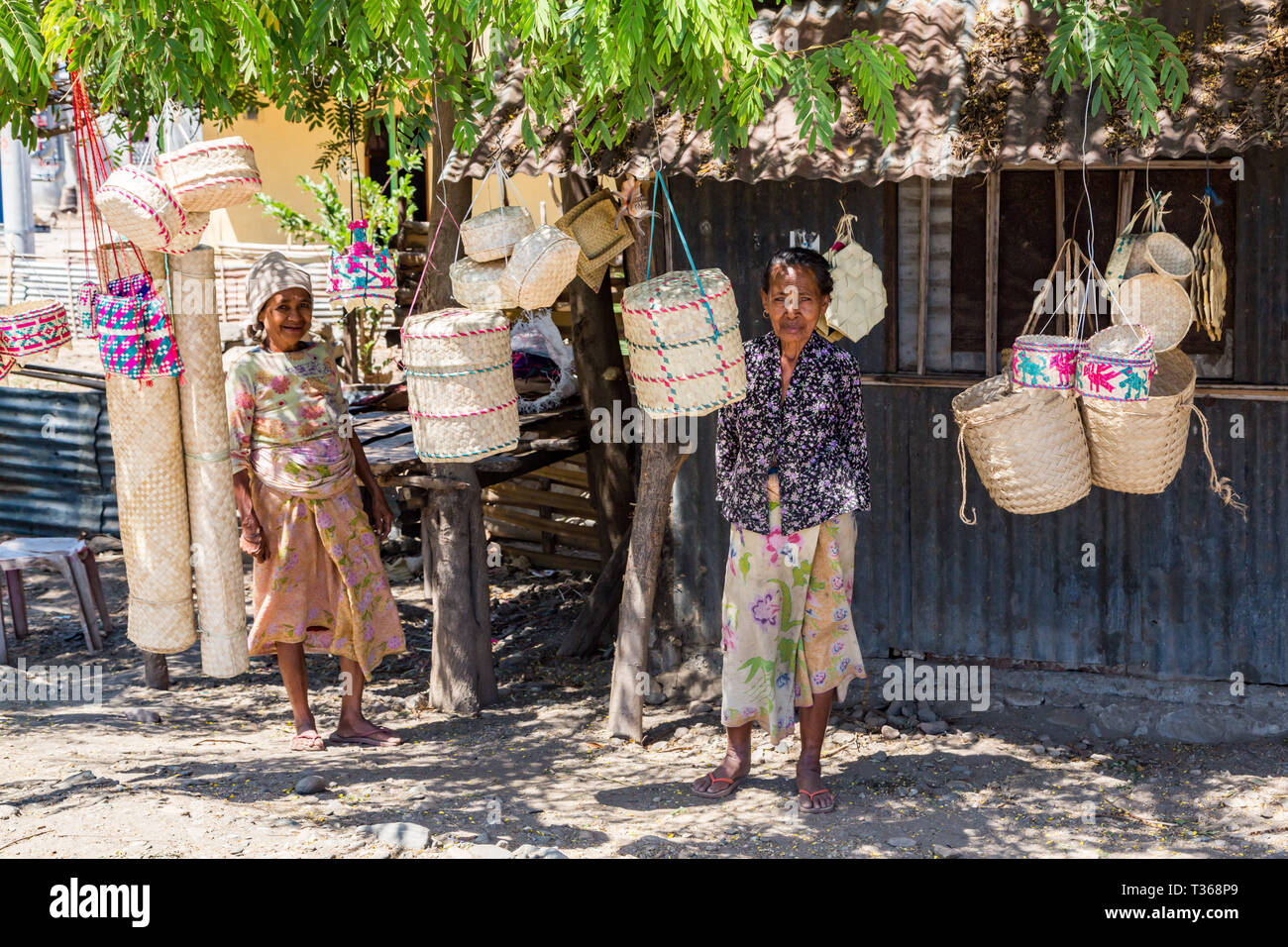 Dili, Timor-Leste - Aug 11, 2015: Two local elderly native East Timorese women, street vending traditional wicker baskets hanging on ropes, at a tin h Stock Photo