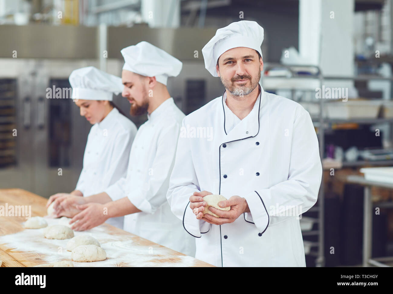 Baker against the background of workers in the bakery. Stock Photo