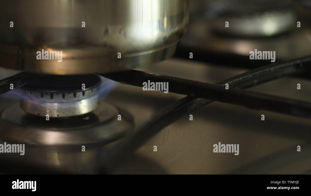 A man or woman lights a fire on an automatic electric ignition on an advanced gas stove and puts on it a metal pan. slow motion close up in 4K. Stock Photo