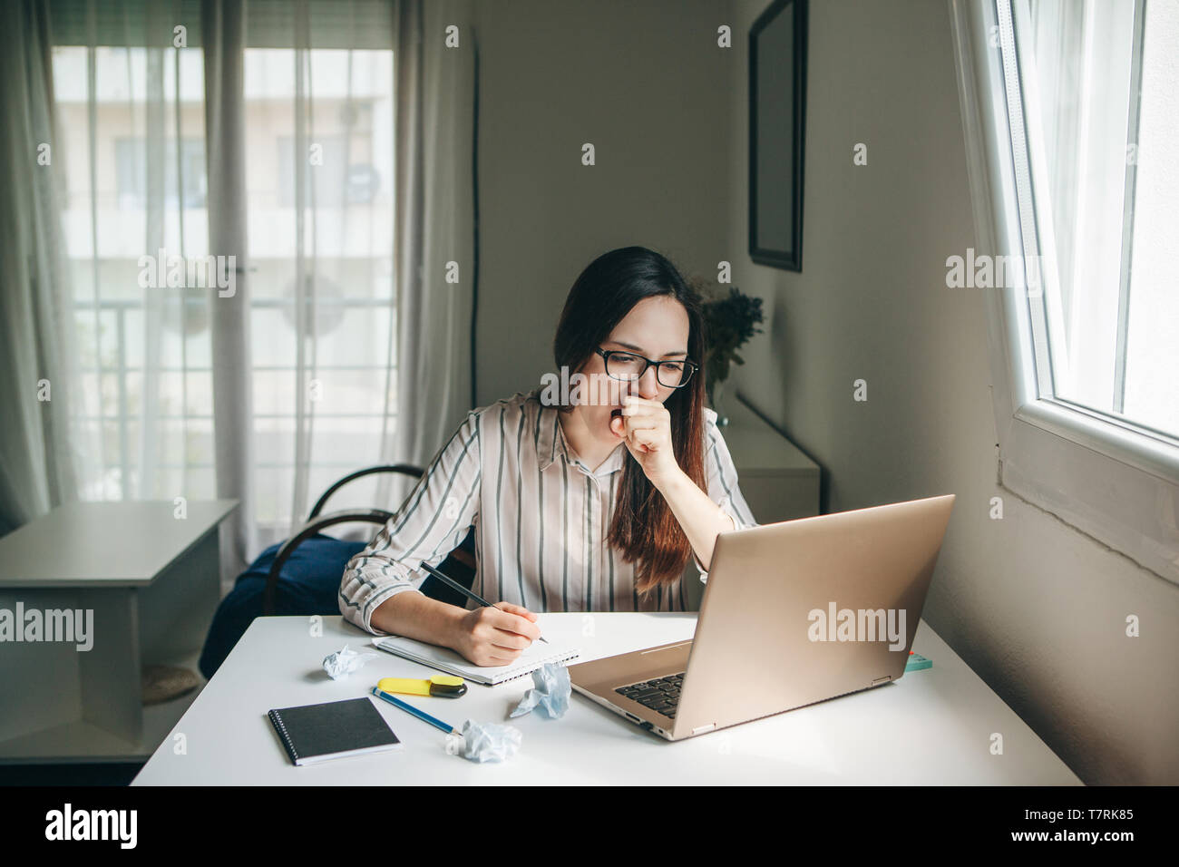 A girl works at a computer in a home office or a student at home teaches lessons. She is tired, yawns and wants to sleep or is bored. Stock Photo