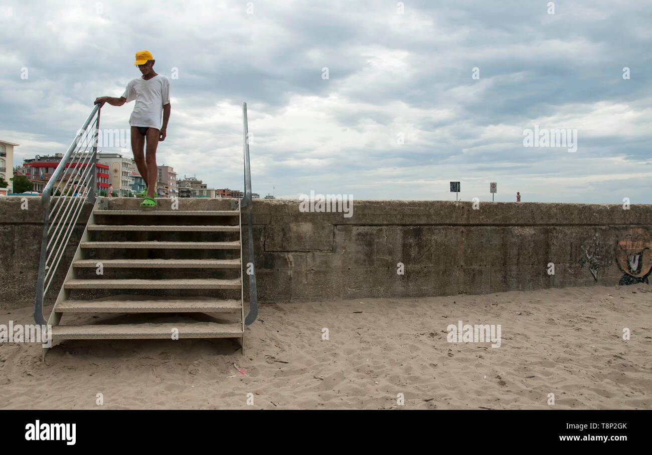 Old man coming down the stairs at the beach Stock Photo