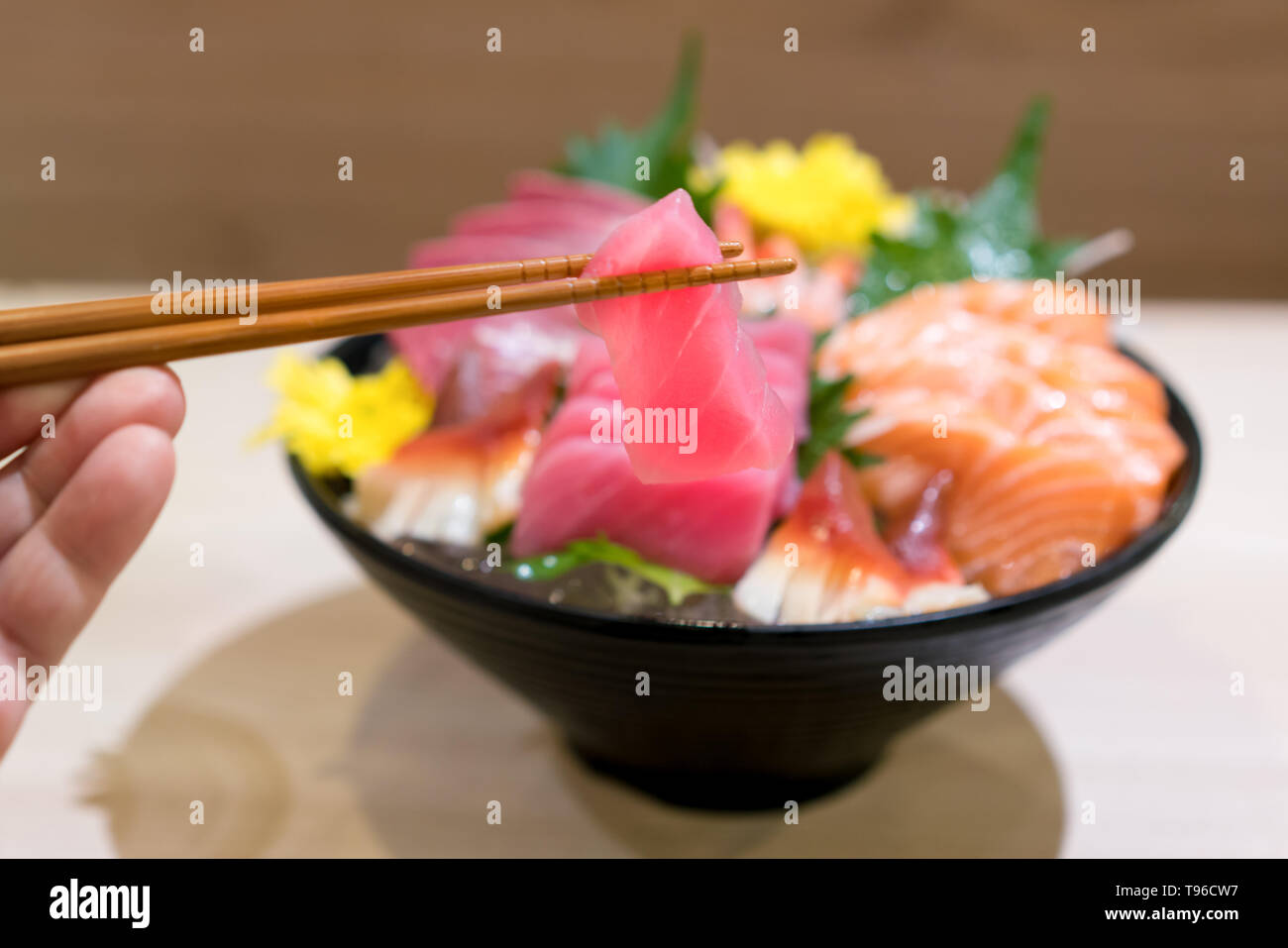 Chopsticks with Tuna sashimi with Mixed sliced fish sashimi on ice in black bowl. Sashimi Salmon Tuna Hamachi Prawn and Surf Calm set, raw fish, japan Stock Photo