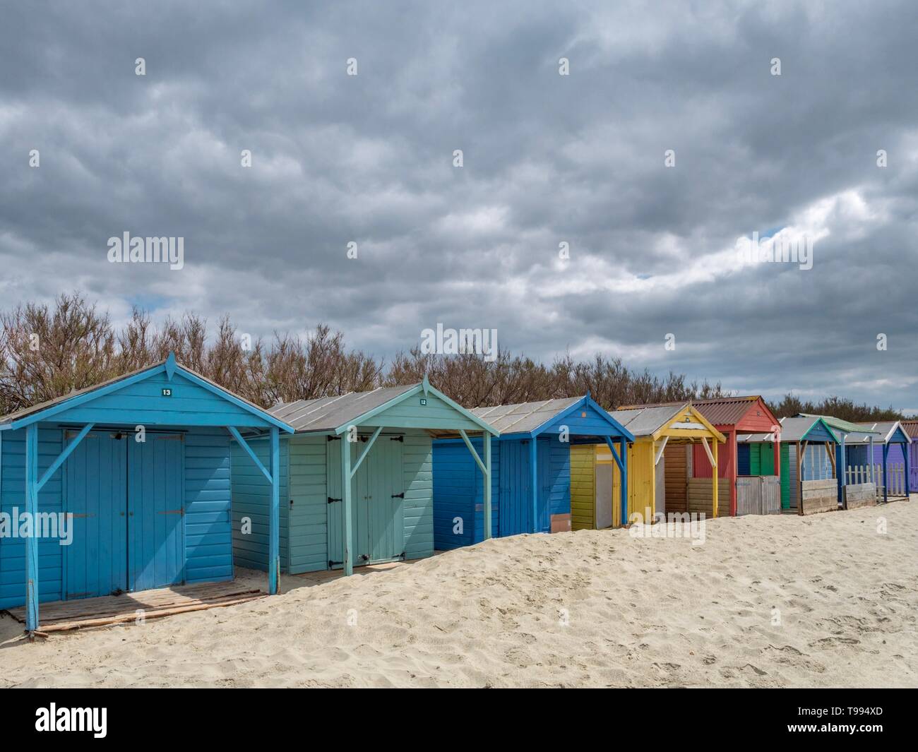 A row of colorful wooden beach huts on a sandy beach in the South of England on a cloudy day Stock Photo