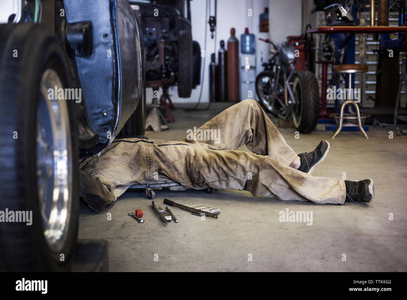 Side view of mechanic on creeper dolly while working under car in auto repair shop Stock Photo