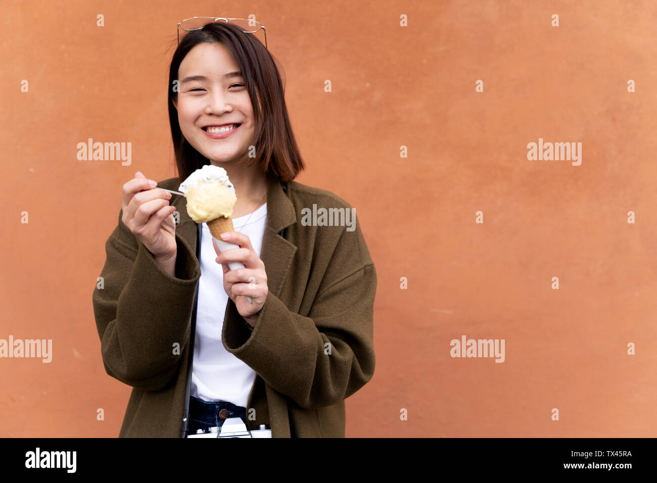 Happy young woman eating an ice cream cone at an orange wall Stock Photo