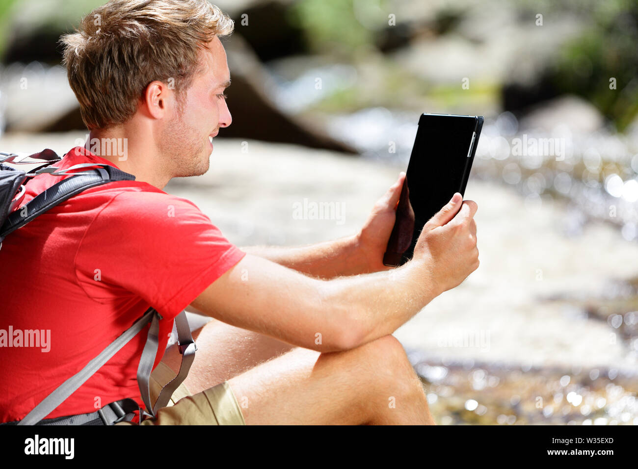 Tablet computer man hiker hiking in Yosemite, USA using travel app or map during hike, resting by river. Caucasian male hiker relaxing on a summer day. Stock Photo