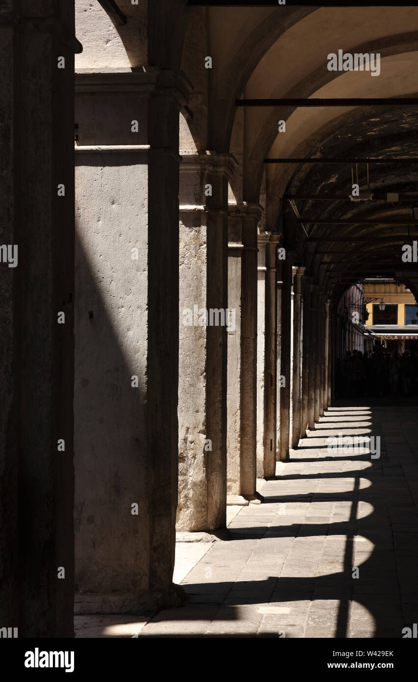 Portrait view of columns and arches with shadows surrounding a small square, Venice, Italy Stock Photo