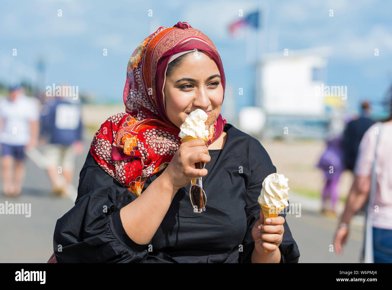 Young Asian woman eating a 99 ice cream at the seaside in Summer in the UK. Stock Photo