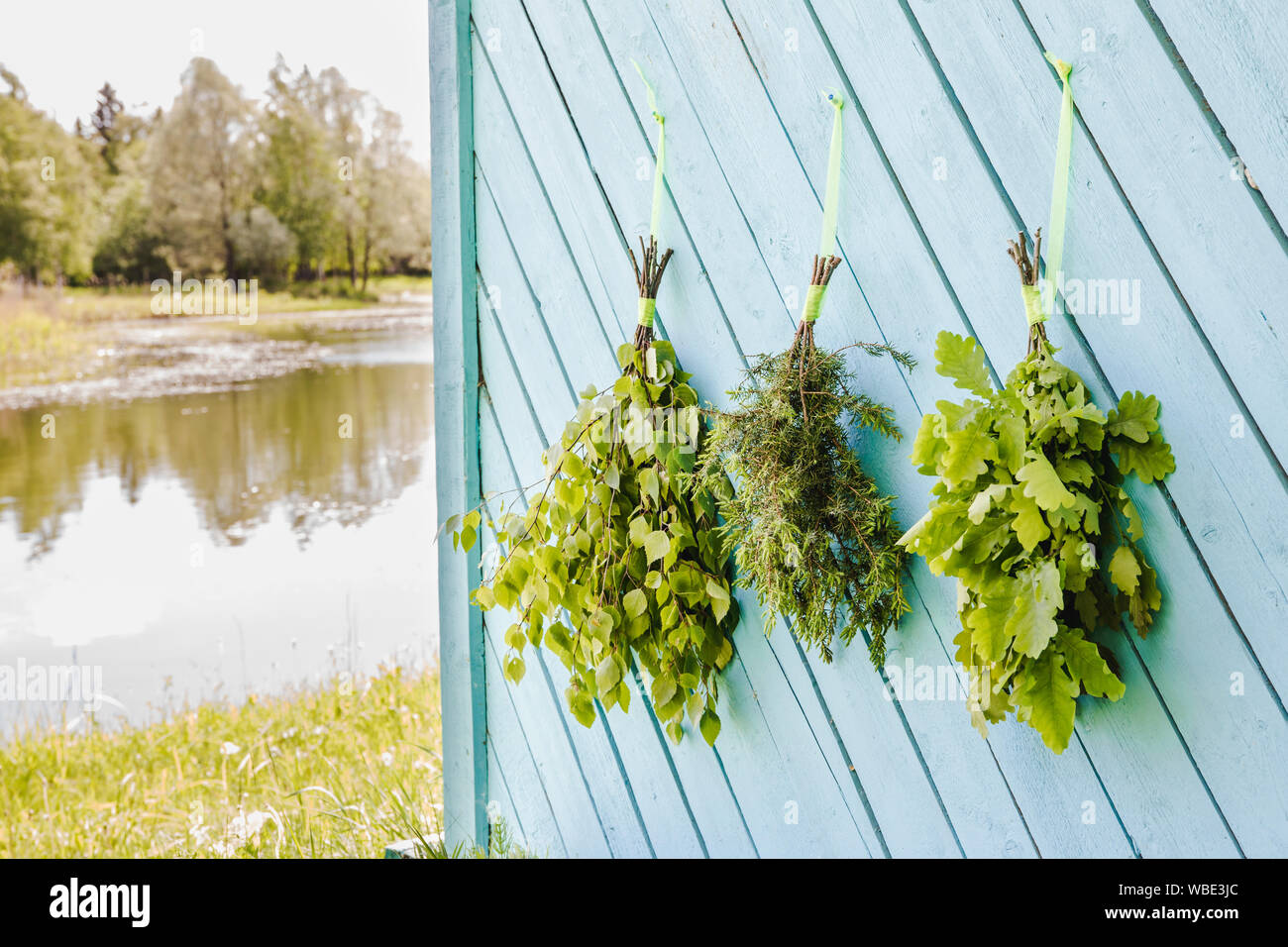 Fresh oak, birch, juniper and oak tree sauna whisks brooms hanging and drying on sauna house wall by beautiful natural lake. Traditional Finnish sauna Stock Photo