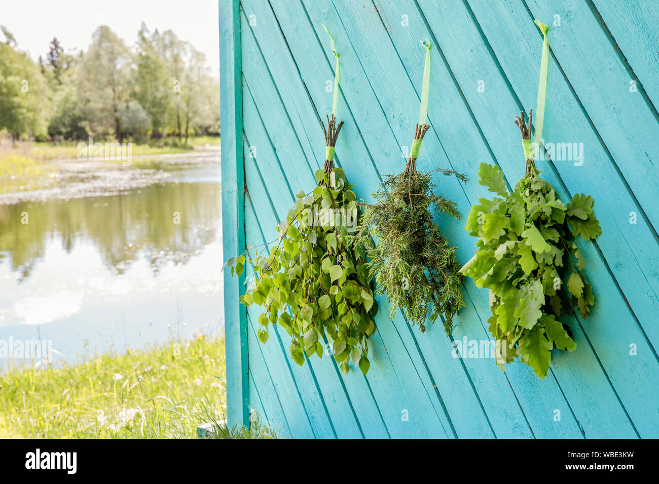 Fresh oak, birch, juniper and oak tree sauna whisks brooms hanging and drying on sauna house wall by beautiful natural lake. Traditional Finnish sauna Stock Photo