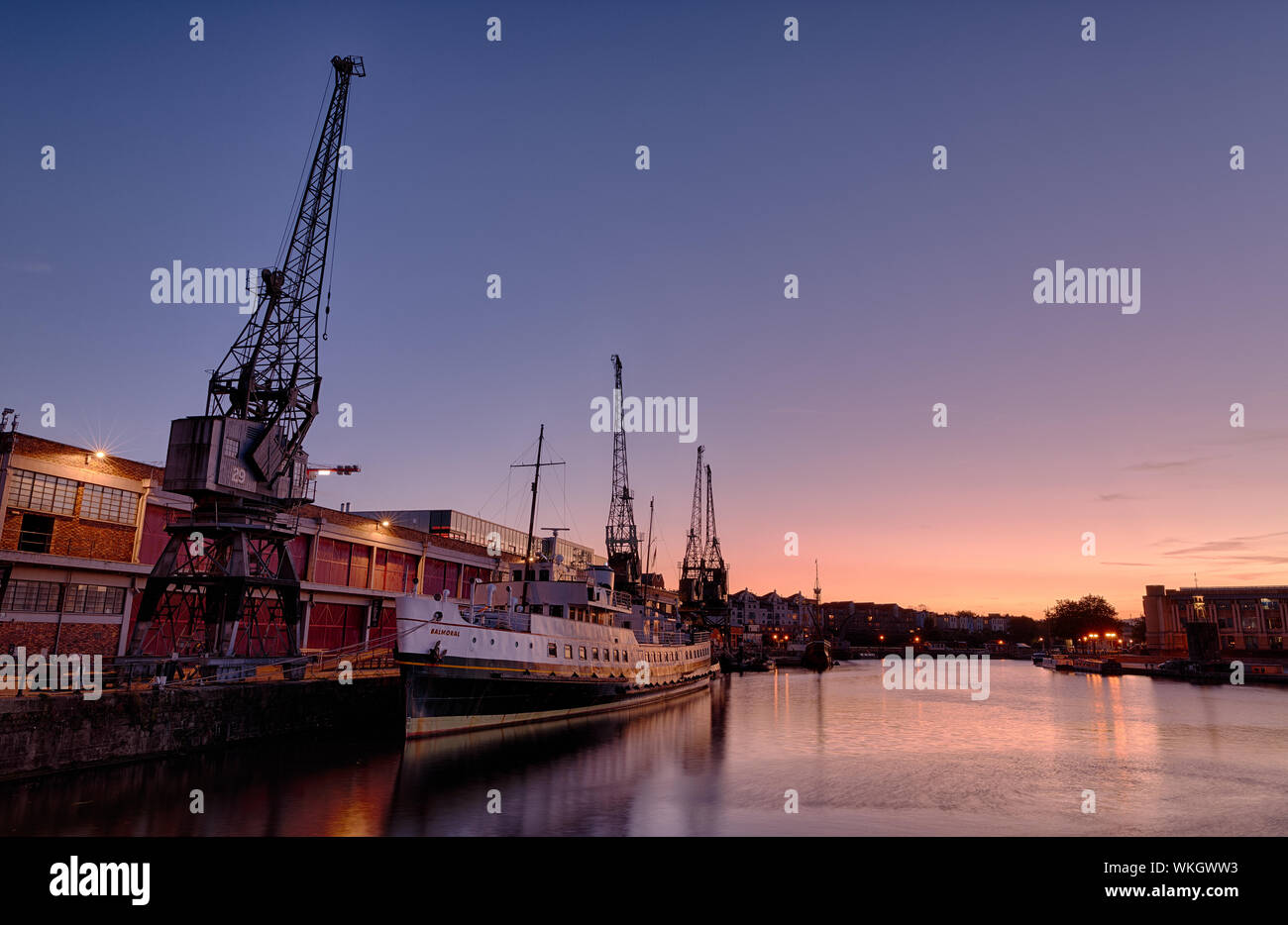 Bristol's floating harbour at sunset. In the foreground is a ship, the Balmoral. Next to it are the M-Shed cranes, disappearing down quayside. Stock Photo