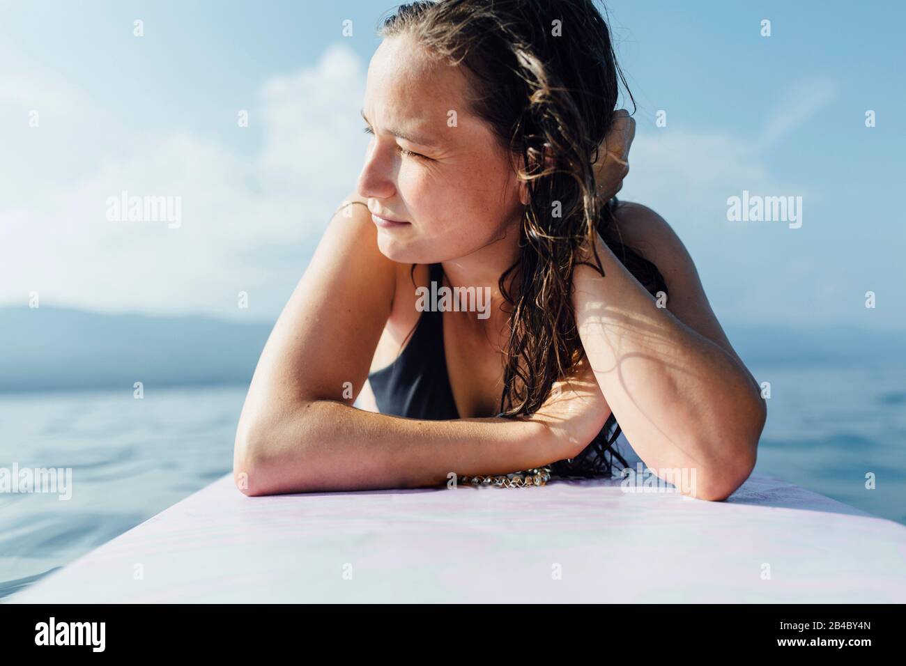 Junge Frau 20-30 Jahre liegt auf Surfbrett und genießt die Sonne, Kroatien Banque D'Images