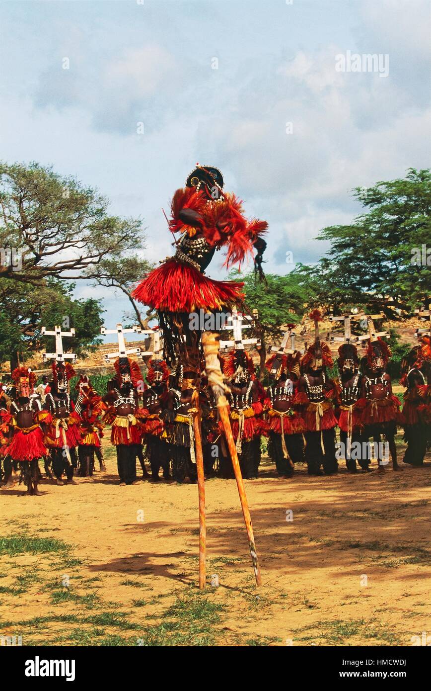 Danzatori Dogon, uno di essi su palafitte, indossando maschere Kanaga eseguendo la Dama o mascherato danza funebre, Bandiagara scarpata, Foto Stock