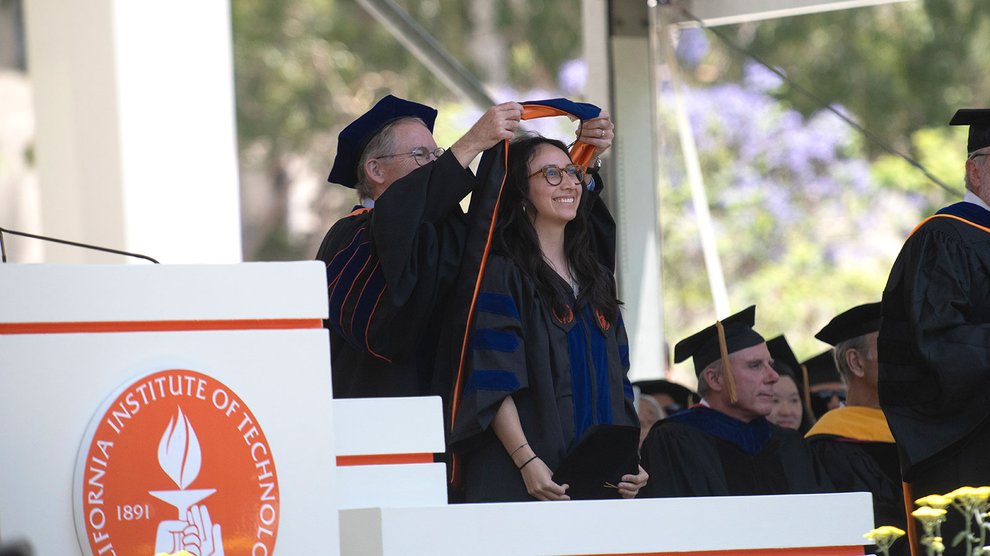 A doctoral graduate is hooded on stage.