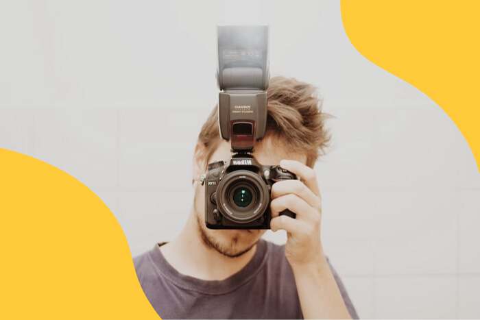 A guy holding a camera with flash towards the photographer