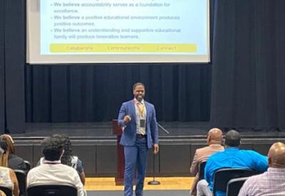 Dr. Eubanks speaking to a crowd with a monitor hanging from the ceiling