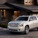 A light colored 2019 GMC Yukon XL Denali is parked in front of a modern house.