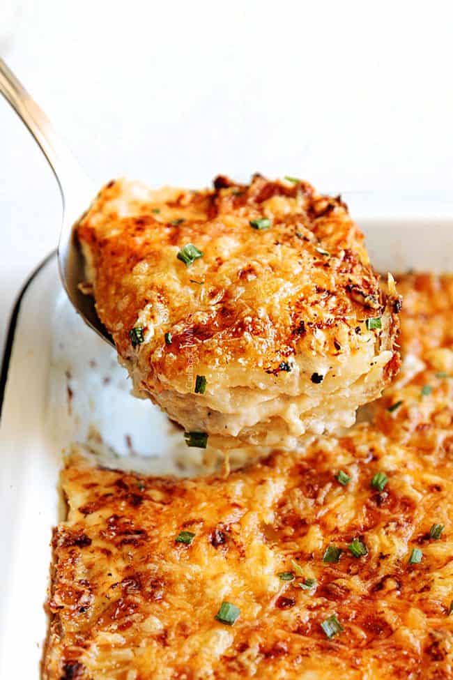 Potatoes Au Gratin with layers of potatoes, cheese and cream in a white casserole dish being scooped up