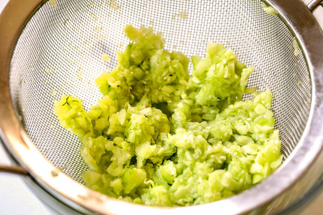 showing how to make Tzatziki by draining cucumbers in a fine mesh sieve to get rid of moisture