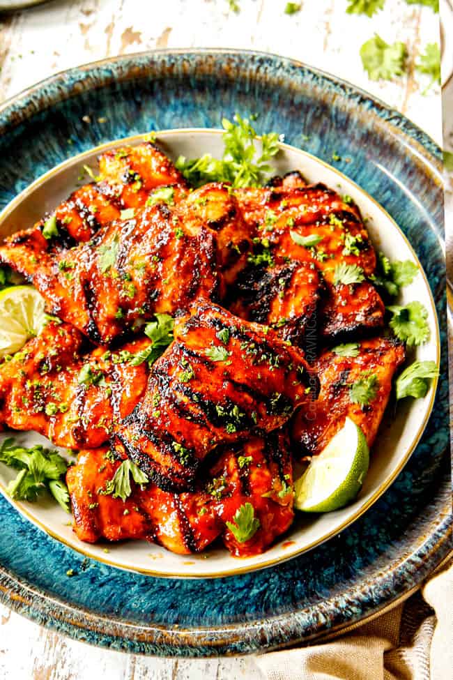 showing how to serve Honey Sriracha Chicken by piling it on a cream plate with limes