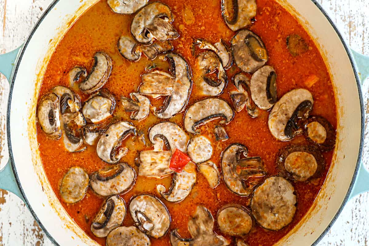 showing how to make Thai coconut curry soup with chicken by adding mushrooms, bell peppers and rice to the soup