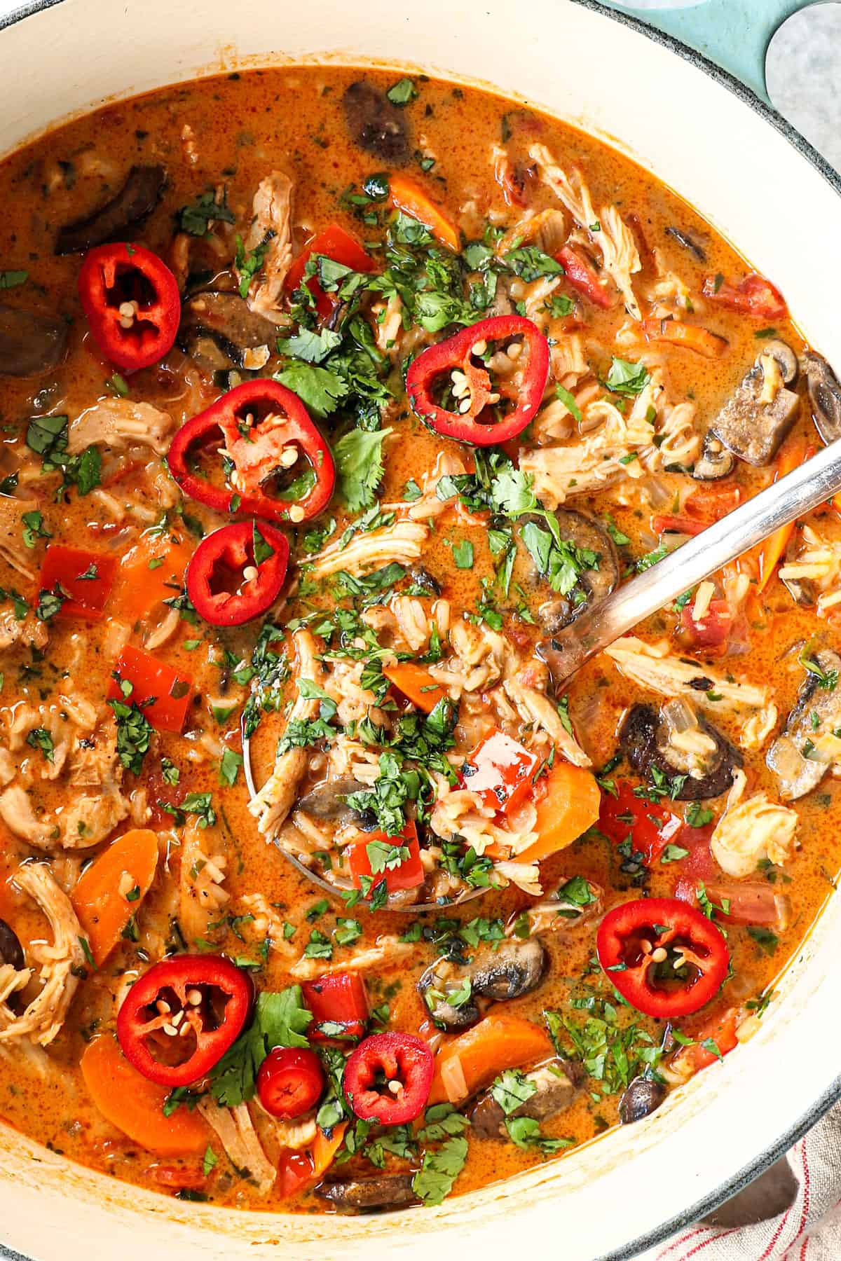 top view of serving coconut curry sup with chicken in a Dutch pot garnished with cilantro and chili peppers