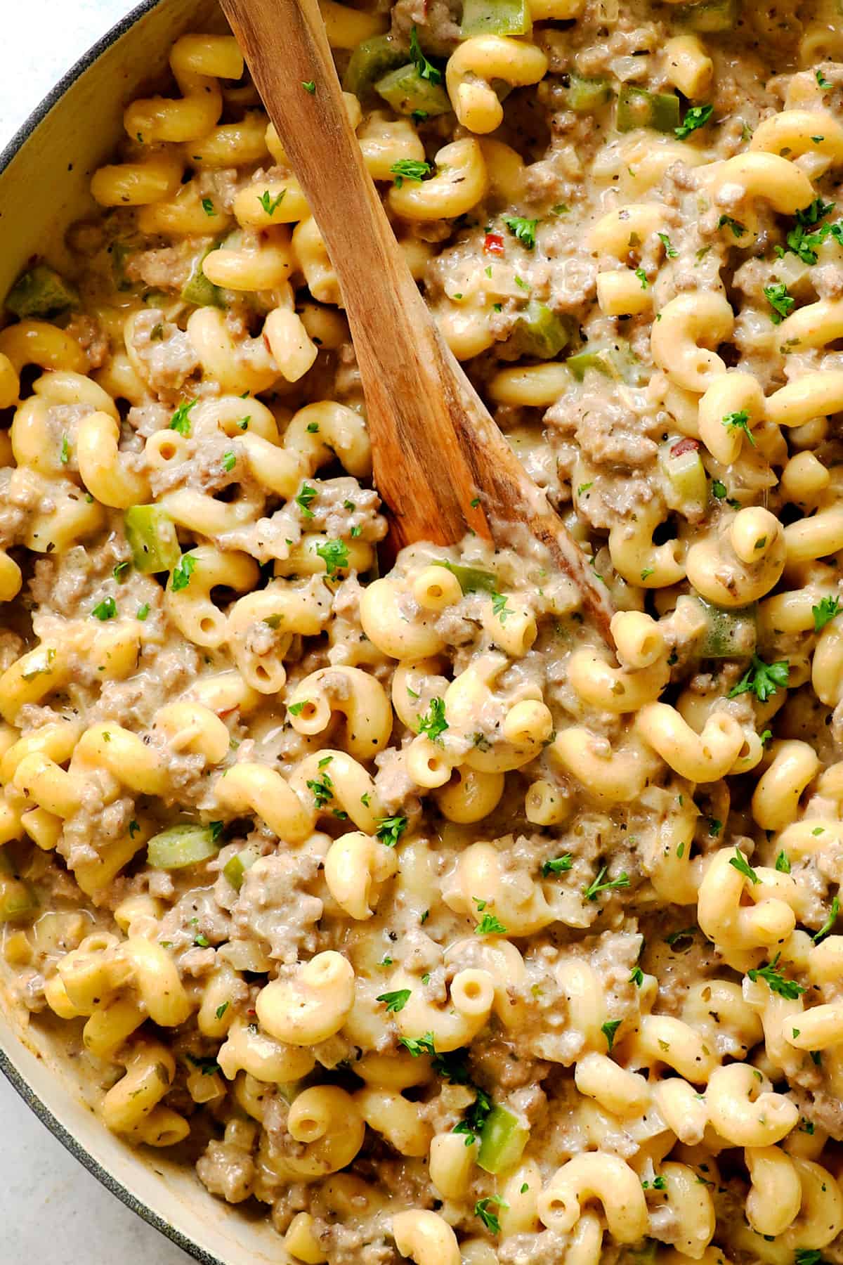 showing how to make Philly Cheesesteak Pasta by stirring cheese into the ground beef pasta 