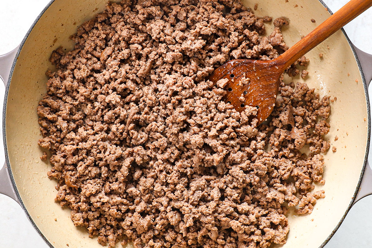 showing how to make Philly Cheesesteak Pasta by browning ground beef in a pan 